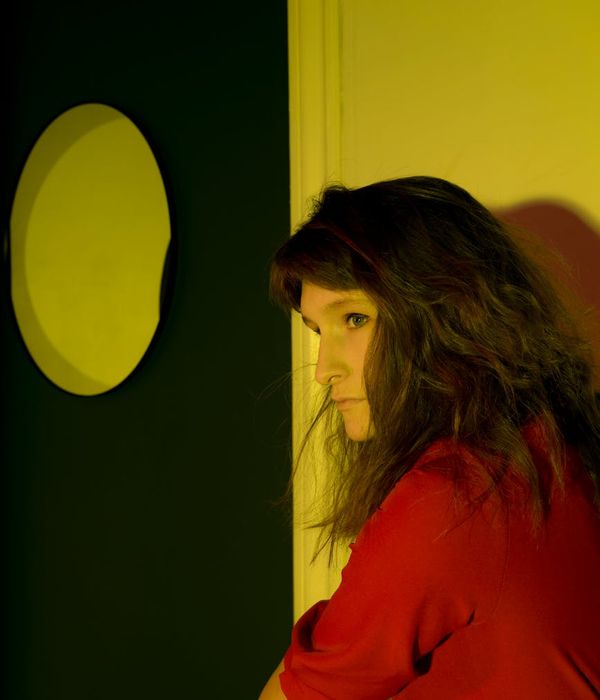 Woman in a calming yoga pose in a dark room with iris colored light.